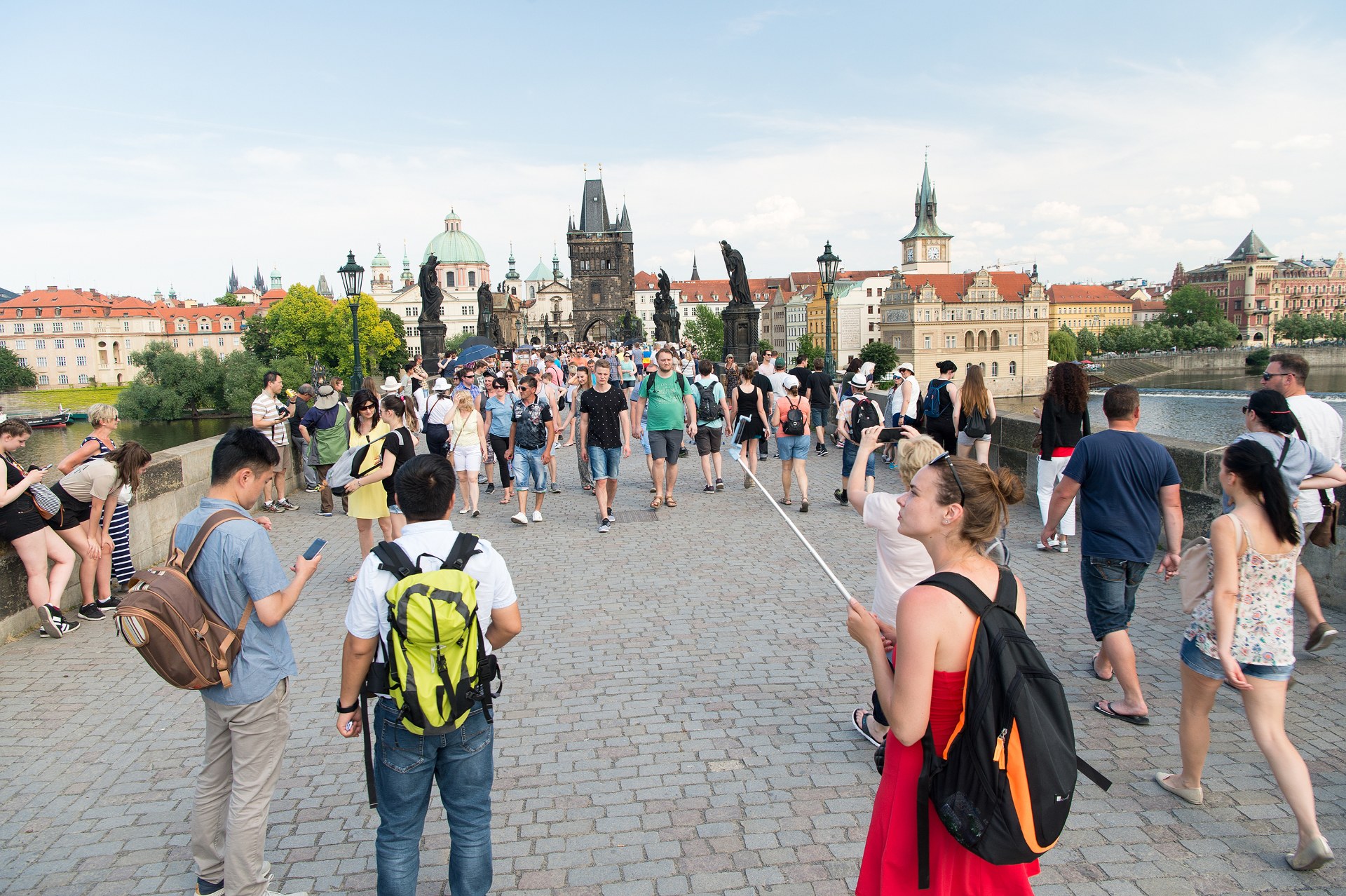 Mladí lidé s batohy přecházejí Karlův most v Praze, za nimi Staroměstská mostecká věž